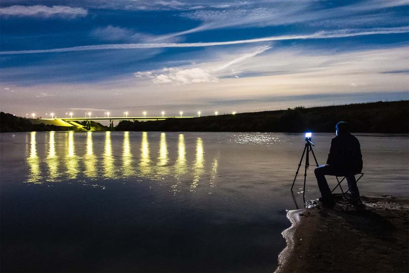 Smartphone tripods Photo of a man standing in front of a smartphone on a tripod, capturing a nighttime landscape