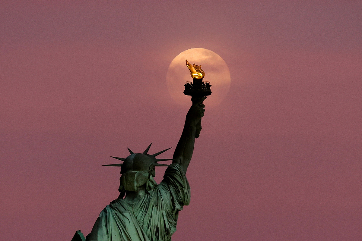 The 2025 Flower Moon rises through clouds above the Statue of Liberty, New York City. Photo by Gary Hershorn/Getty Images