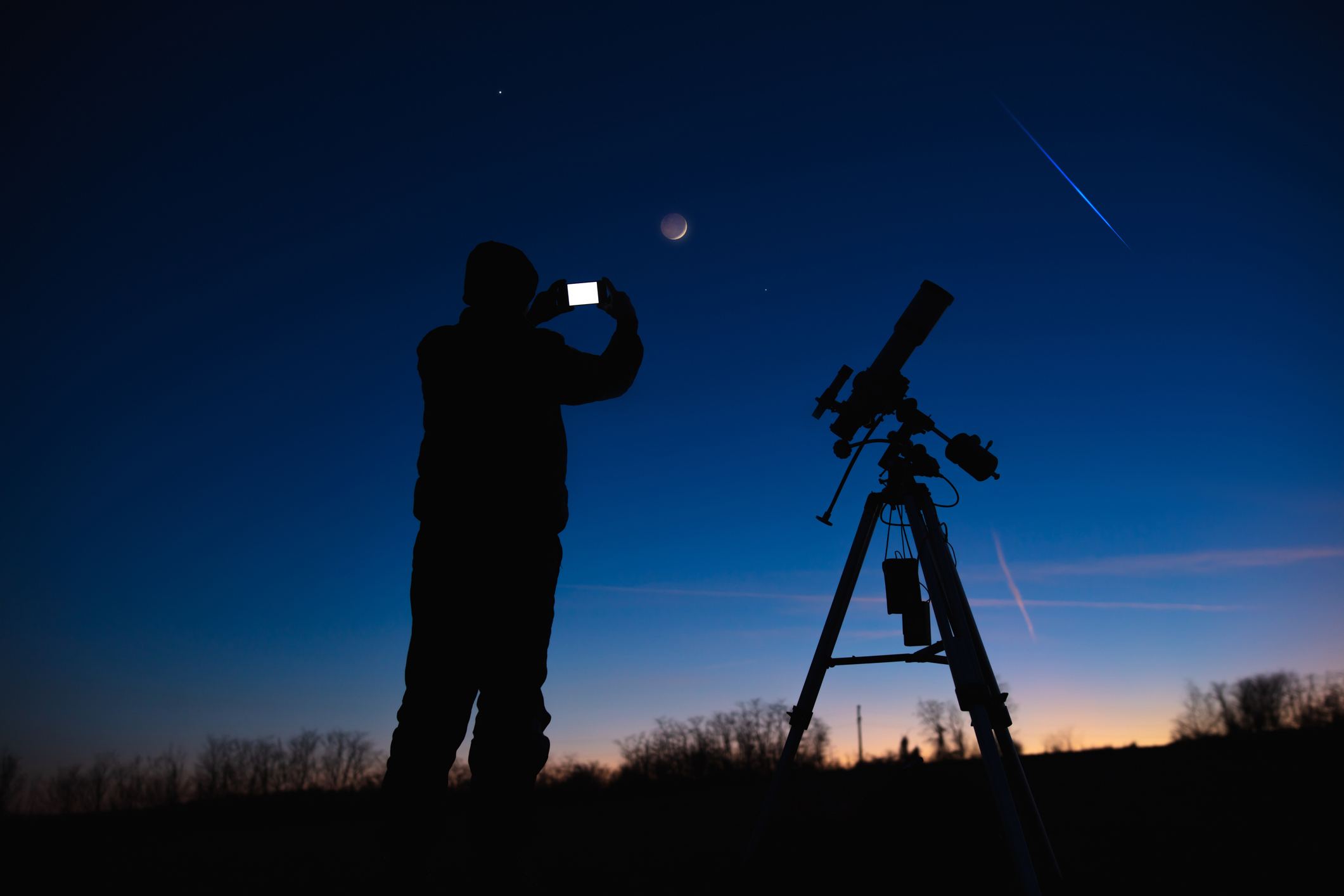 Silhouette of person photographing the Moon with their smartphone