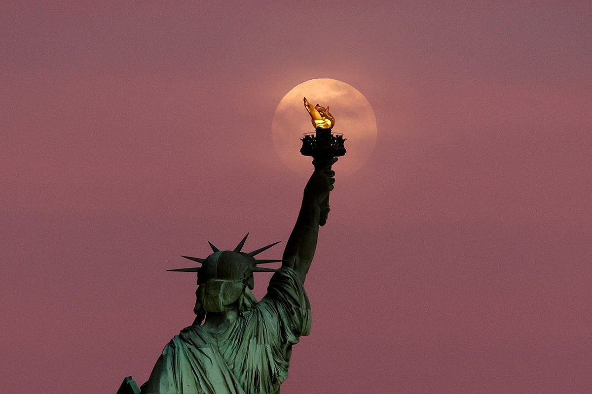 The 2025 Flower Moon rises through clouds above the Statue of Liberty, New York City. Photo by Gary Hershorn/Getty Images